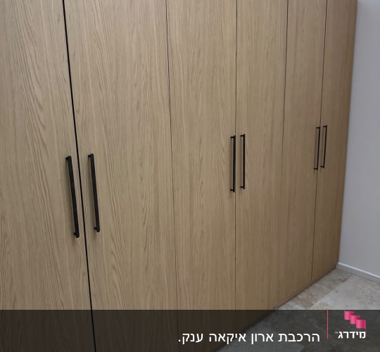 ארון בגדים מעץ עם ידיות שחורות שהורכב בחדר